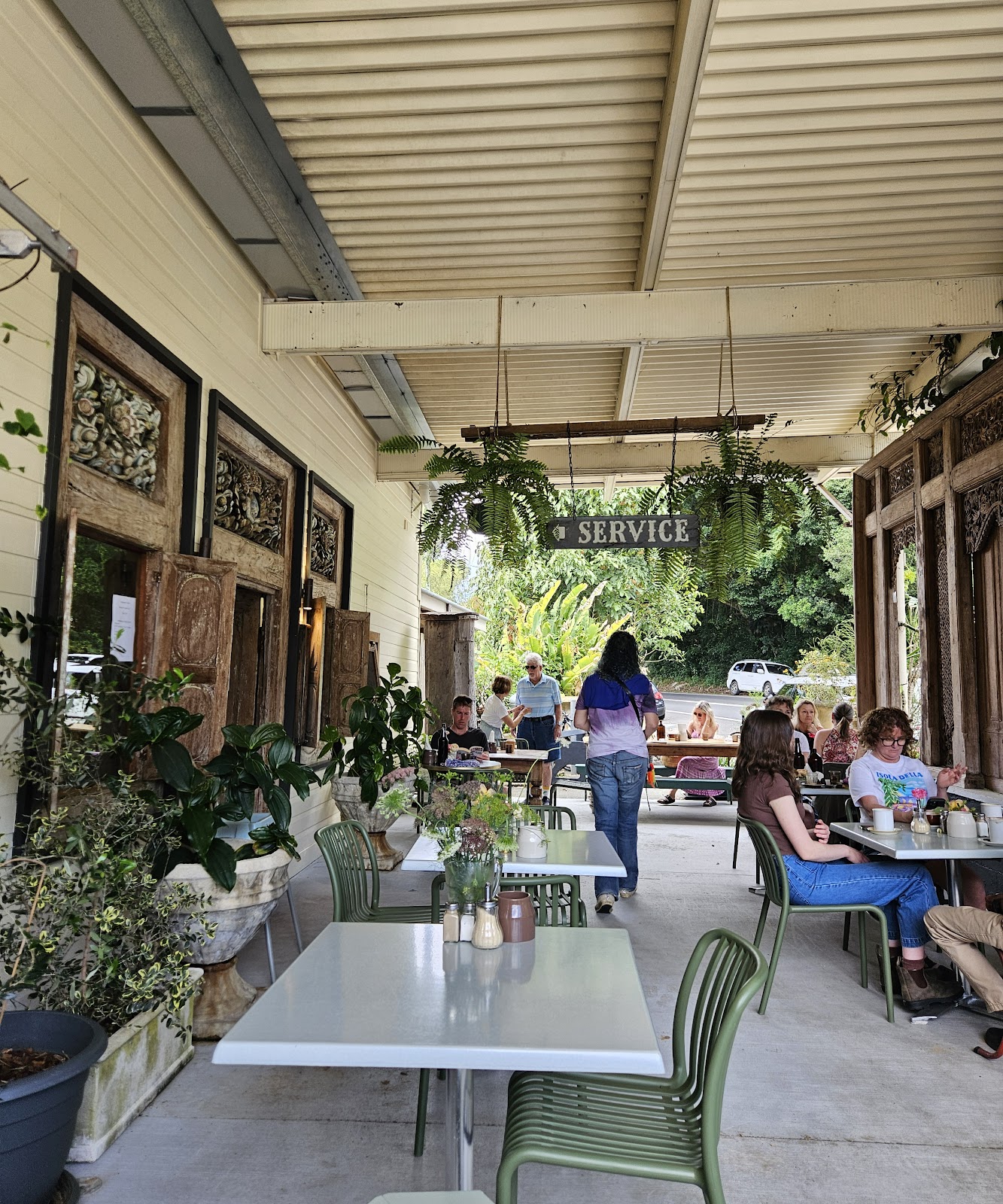 The long verandah at Teakwood Cafe with green chairs, hanging ferns and carved timber doors